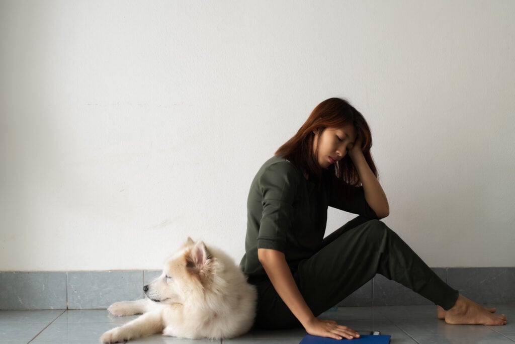 lady looking very sad about her white samoyed puppy laying behind her, does she have the puppy blues?